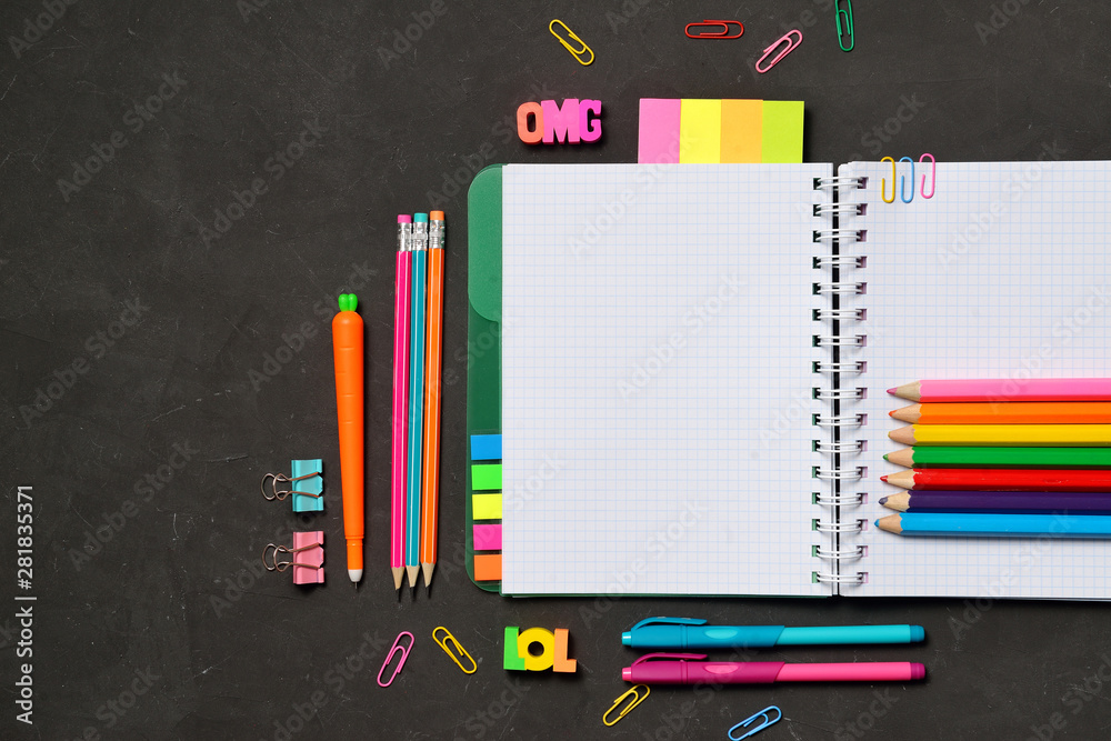 Back to School concept - open copy book with office and student supplies on black chalk background. Space for text.