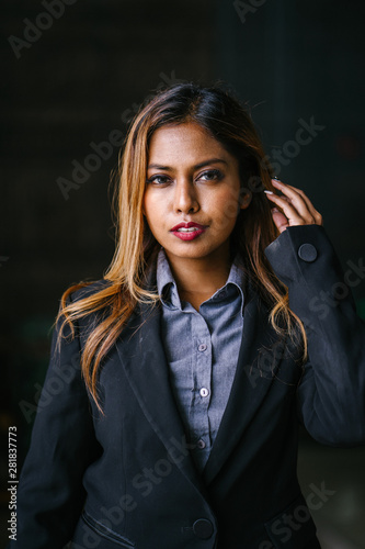 A portrait of a young, tanned, beautiful and confident Southeast Asian business woman. She is smiling confidently and happily. The woman is wearing a suit and is adjusting her hair.