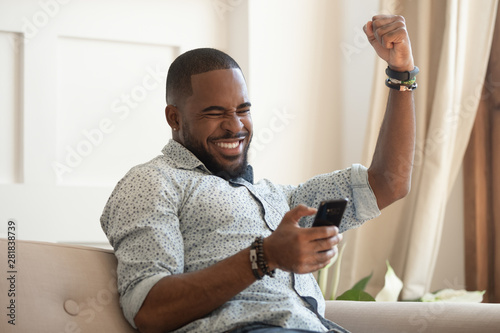 Overjoyed black man holding smartphone feeling euphoric with mobile win
