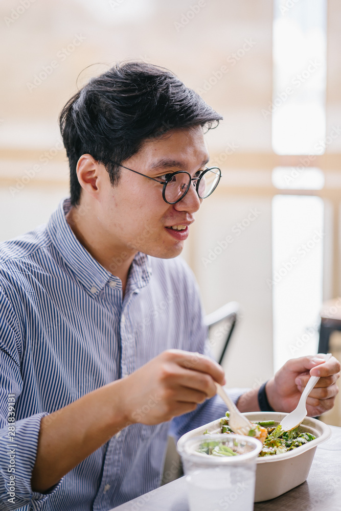 A Korean Asian man enjoys his salad lunch as he sits in a cafe in the city during the day. He is tall, handsome and is wearing a collared shirt and spectacles. A Korean Asian man enjoys his salad lunch as he sits in a cafe in the city during the day. He is tall, handsome and is wearing a collared shirt and spectacles.