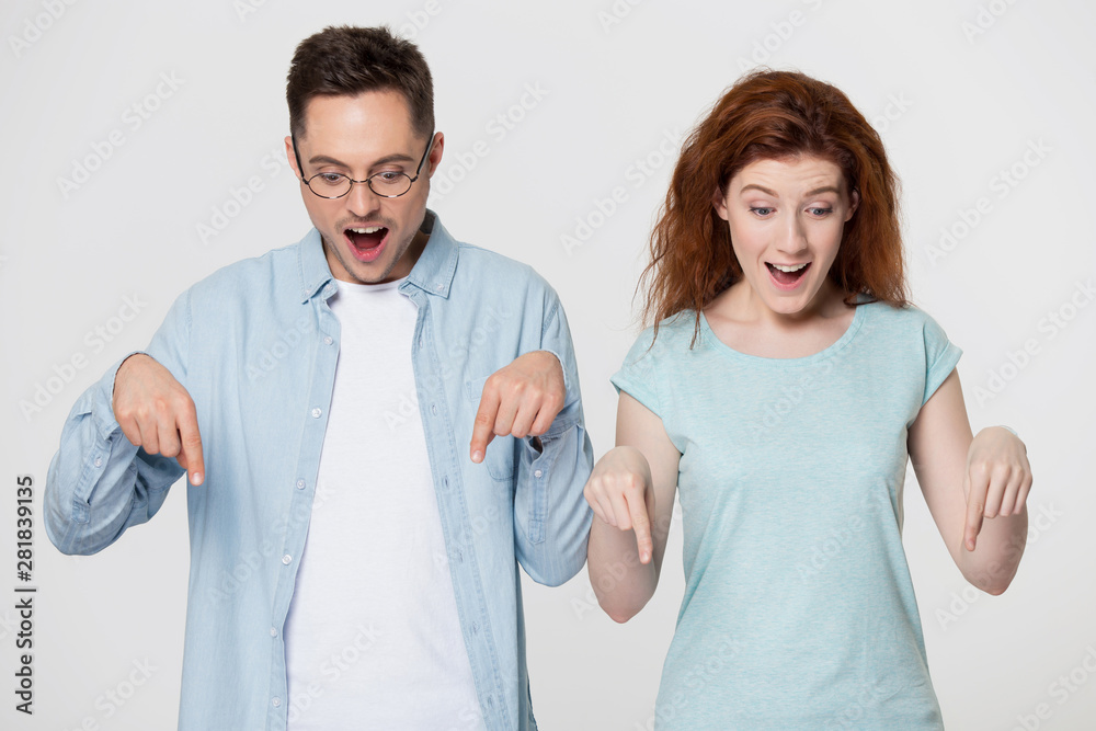 Millennial positive couple feels amazed pointing fingers down studio image Millennial positive couple feels amazed pointing fingers down studio image