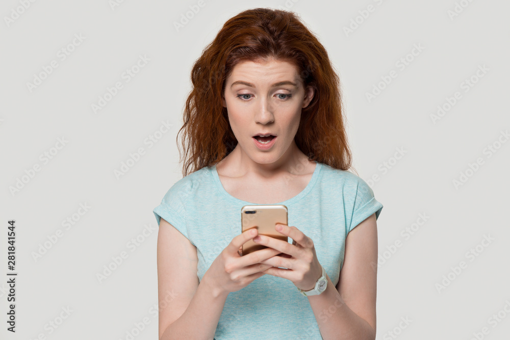 Redhead woman looks at smartphone screen feels shocked studio shot Redhead woman looks at smartphone screen feels shocked studio shot