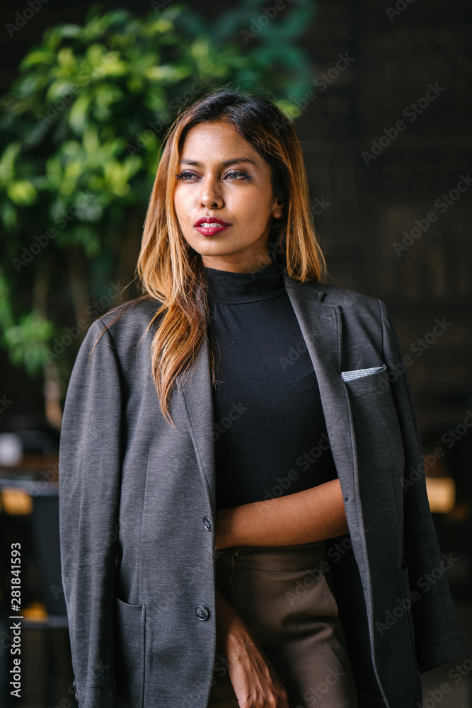 Portrait of a fashionable, capable and confident Southeast Asian woman in the city during the day. She is young, attractive and wearing a black turtleneck, khakis and has a jacket over her shoulders.