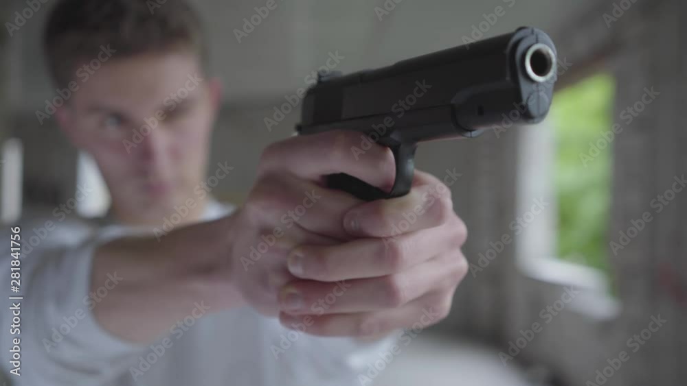 Young defocused man aiming with the pistol, his hands shaking close-up. The guy is going to kill the human in an abandoned building Young defocused man aiming with the pistol, his hands shaking close-up. The guy is going to kill the human in an abandoned building
