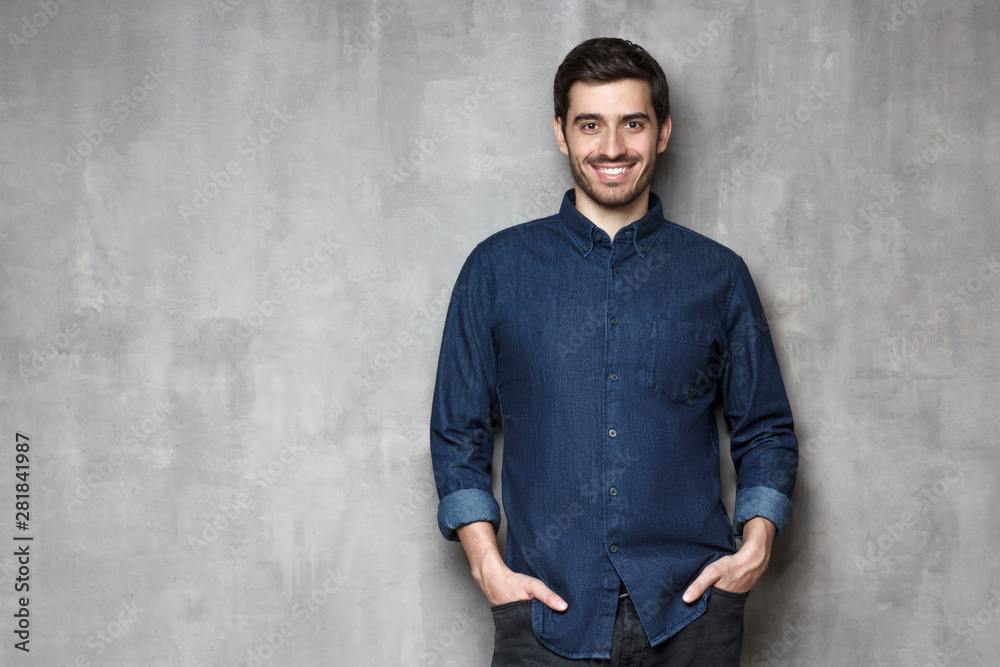 Young business man satisfied with his life standing against gray wall with copy space on left side