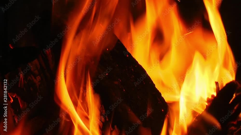 Close-up Shot of Firewood Burning features a close-up shot of a pile of firewood burning. It shows small golden flames consuming the wood and the background is dark. Close-up Shot of Firewood Burning features a close-up shot of a pile of firewood burning. It shows small golden flames consuming the wood and the background is dark.