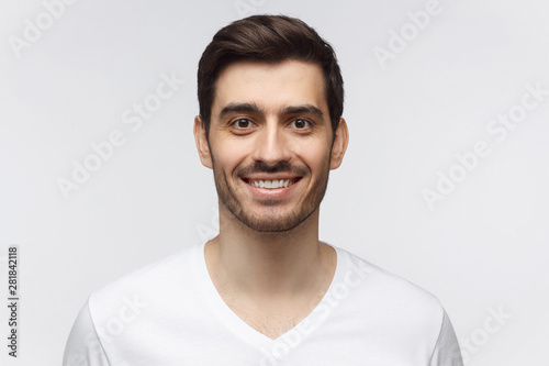 Portrait of smiling handsome young man in white t-shirt, looking at camera, isolated on gray background