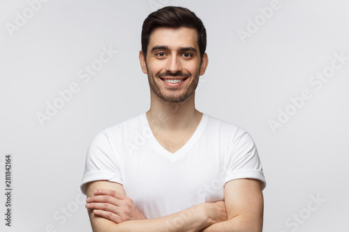 Portrait of smiling man in white t-shirt standing with crossed arms, isolated on gray