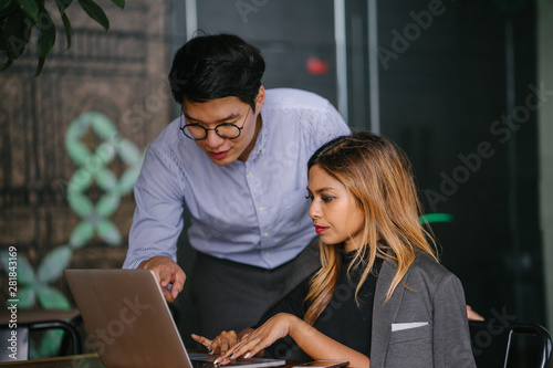 Candid shot of two young Asian businesspeople having a consultation for a business advice while sitting in a trendy coworking space during the day in the cafeteria. 