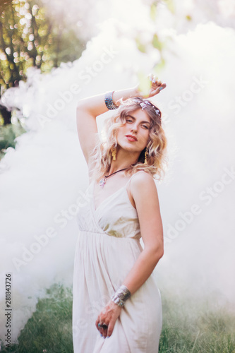 Bohemian hippie girl in white dress. Woman with boho style jewelry. Colored smoke on background.Coachella Bohemian Look. Spirit of freedom.