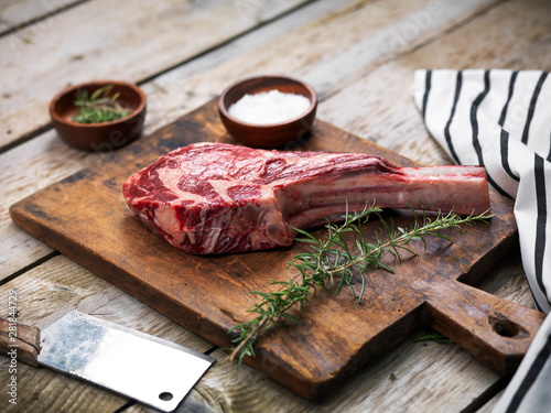 Raw fresh angus meat tomahawk on a wooden cutting board with rosemary, salt and butcher's knife photo