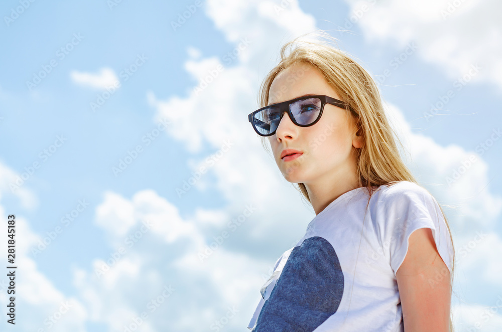 Summer portrait of a blonde girl in sunglasses on a background of the sky with clouds