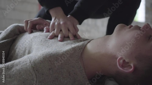 The young man dies in an abandoned building from a drug overdose, lying on a concrete floor close-up. His friend presses his chest and checks the pulse on his neck. Danger of drug addiction