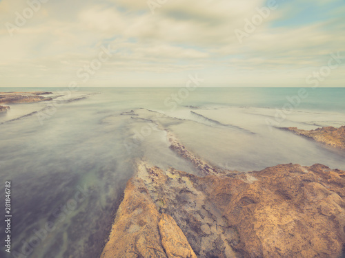 seascape at sunset with beach of rocks beaten by the sea and clouds moving in the sky