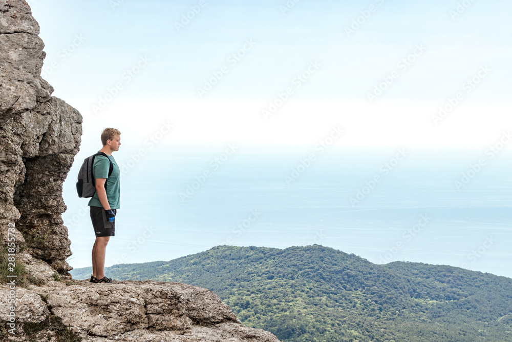 Young man with a backpack on top of cliff enjoying view of nature. Mountains and sea