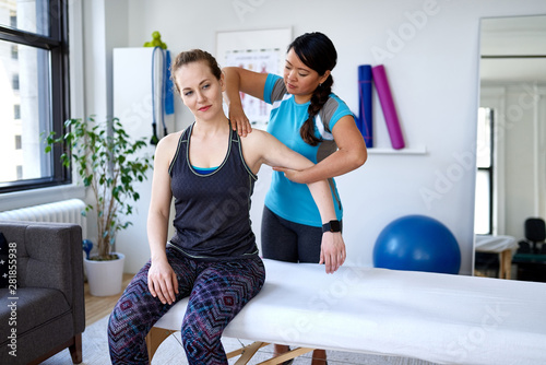 Chinese woman physiotherapy professional giving a treatment to an attractive blond client in a bright medical office photo