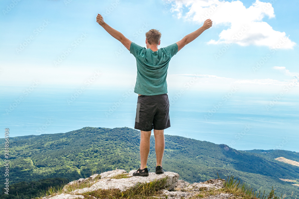 Young man standing on top of cliff in mountains and enjoying view of nature. Mountains and sea Young man standing on top of cliff in mountains and enjoying view of nature. Mountains and sea
