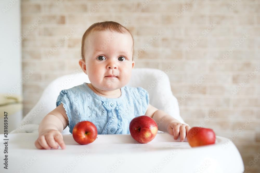 Cute baby girl eating apple in the kitchen. Little kid tasting solids at home. Healthy nutrition for kids. copy space Cute baby girl eating apple in the kitchen. Little kid tasting solids at home. Healthy nutrition for kids. copy space