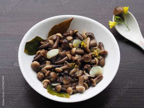 Excellent and beautiful pickled mushrooms and spices in a white plate, one fungus in a spoon on a wooden background. Home recipe pickles - small mushrooms with garlic and herbs close-up.