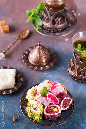 Obraz na płótnie Bowl with various pieces of turkish delight lokum and black tea with mint on a dark background