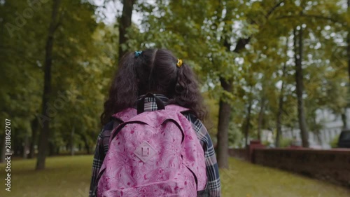 Back view of schoolgirl with bagpack walking in the park. Back to school concept. Slow Motion Shot.