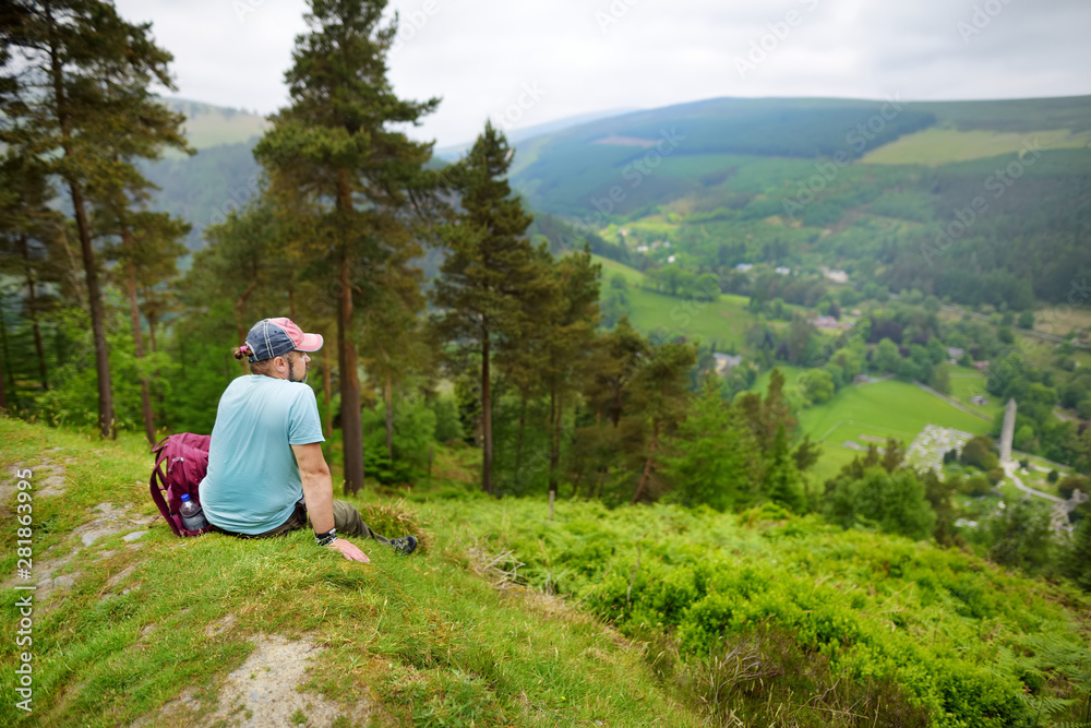 Naklejka premium Tourist exploring the woodlands of Wicklow Mountains National Park. Old pine trees and lush greenery of Glendalough valley, County Wicklow, Ireland