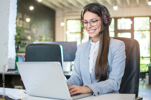 Smiling female customer support operator talking with client and using laptop in office photo