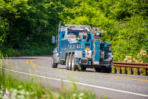 Powerful big rig towing truck for tow semi trucks running on the winding road in green forest