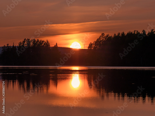 Sunset in Swedish coutry side landscape. The lake is mirroring the forest and sun.