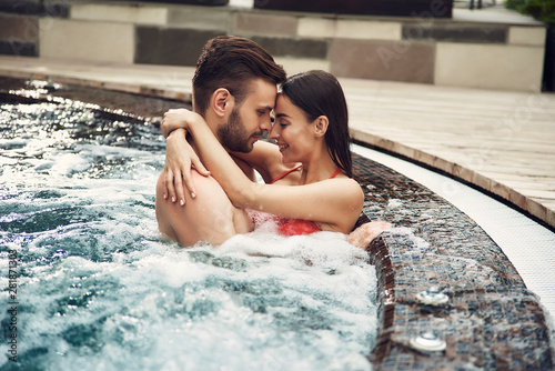 Bearded man and black-haired woman hugging in swimming pool