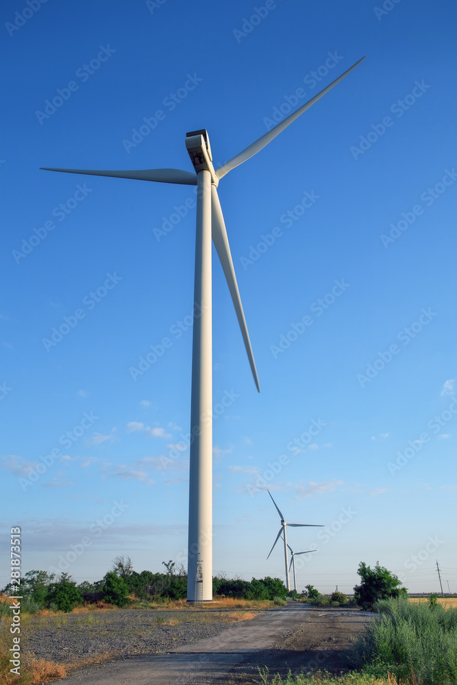 Wind turbines and agricultural field on a summer cloudy day. Energy production, clean and renewable energy. Wind turbines and agricultural field on a summer cloudy day. Energy production, clean and renewable energy.