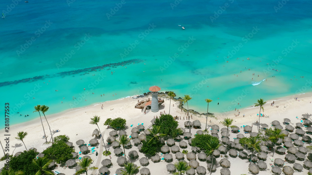 Top view of a palm beach in the Dominican Republic. Blue turquoise sea and white sand on the background. Sunny summer day in the Atlantic Ocean. Beach umbrellas from leaves of coconut palms.