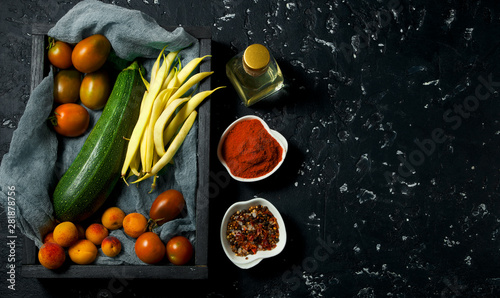 Vegetables on a dark background. Spices, oil, zucchini, asparagus, beans, tomato, peaches on a dark textured surface. View from above. copy space.