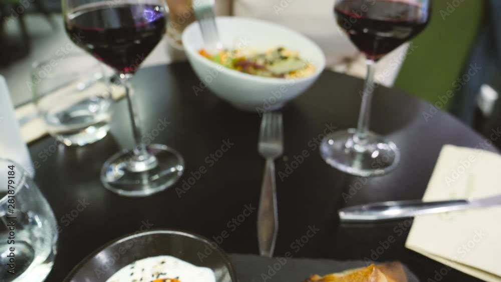 Side view of woman using fork knife eating delicious vegan bio organic food inside inside restaurant - two glasses of wine Side view of woman using fork knife eating delicious vegan bio organic food inside inside restaurant - two glasses of wine