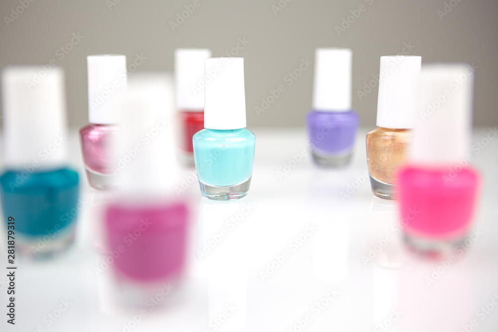 View on a shiny white desk full of small glass and plastic bottles with assorted nail polish and lacquer with focus on one blue nail polish.
