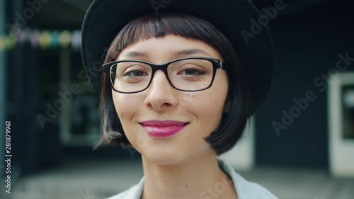 Close-up portrait of young pretty girl in glasses and hat smiling outdoors looking at camera weith cheerful face. Modern people, emotions and happiness concept. photo