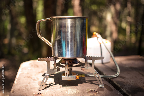 Making tea and coffee in a mug with a gas cooker on top of the wooden table in the middle of the forest at the campground. Warm and summer day