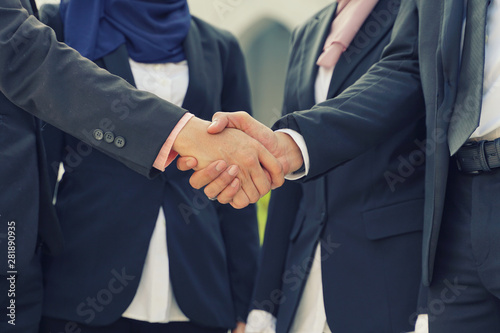 Muslim Asian business people shaking hands with new partner, business co-working teamwork concept. Successfull entrepreneur over a blur majestic building photo