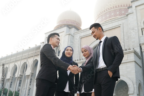 Muslim Asian business people shaking hands with new partner, business co-working teamwork concept. Successfull entrepreneur over a blur majestic building