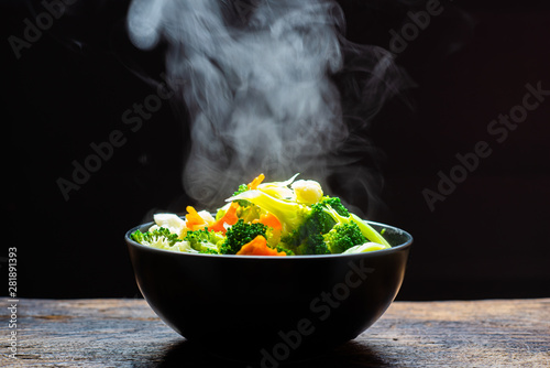 Fototapeta The steam from the vegetables carrot broccoli Cauliflower in a black bowl, a steaming. Boiled hot Healthy food on table on black background,hot food and healthy meal concept
