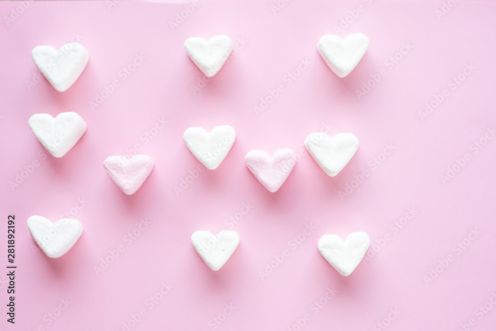 Marshmallow in the shape of a heart on a pink background laid out in a pattern. There is a place for text. Flat lay.