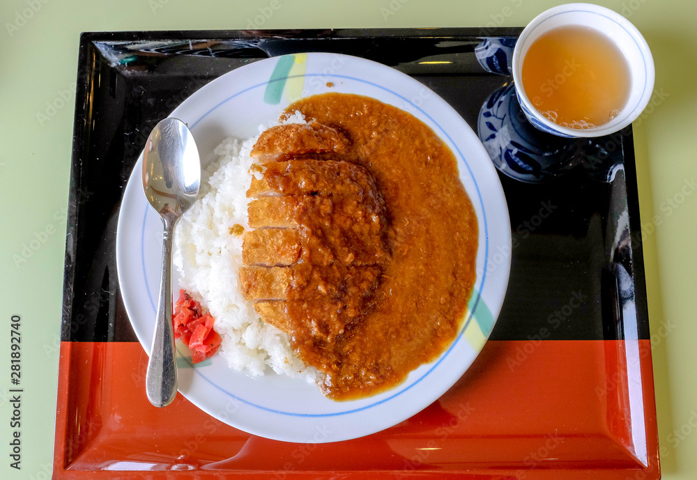White plate of Japanese pork curry or tonkatsu curry,rice on top of fried pork cutlet with soup side dish on black and red tray color, put on table in Japanese restaurant.
