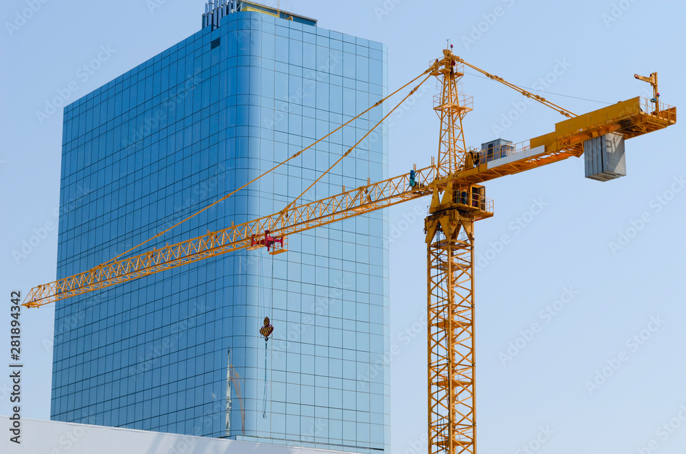 Construction crane on the background of an office building with a mirror surface