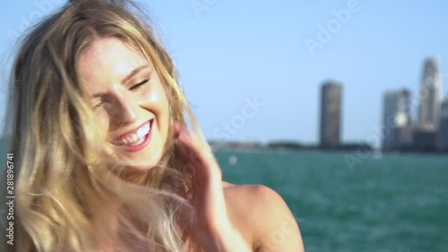 Beautiful Caucasian blonde female with green/blue eyes looks directly into the camera seductively then laughs happily as the wind blows her hair. the Chicago rivers flows towards the tourist city