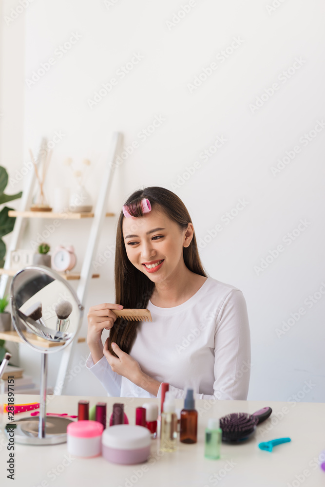Hairstyle tutorial. Asian woman brushing her hair and smiling pleasantly while filming a tutorial for her beauty blog Hairstyle tutorial. Asian woman brushing her hair and smiling pleasantly while filming a tutorial for her beauty blog