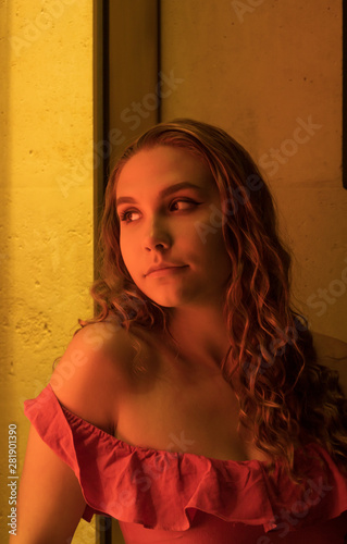 Pretty young blonde woman with a red dress. Leaning against a showcase with bright yellow lights. Night scene in the city. Pretty girl with long hair.  © Bruno