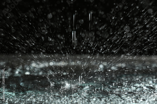 Rain drop falling down into puddle on dark background