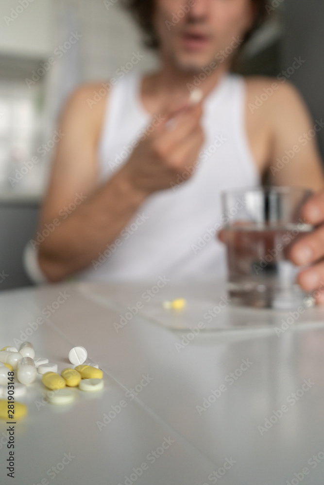 A man holds a glass of water, going to drink pills and tablets lying on the table. Illness, malaise, cold, ache. Front view. Vertical. Close-up A man holds a glass of water, going to drink pills and tablets lying on the table. Illness, malaise, cold, ache. Front view. Vertical. Close-up
