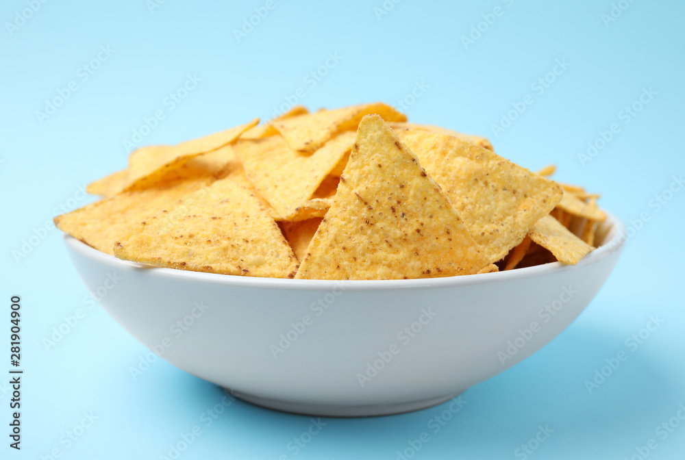 Bowl of tasty Mexican nachos chips on light blue background Bowl of tasty Mexican nachos chips on light blue background