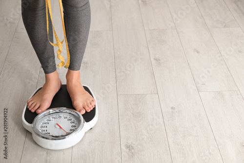 Woman with tape standing on scales indoors, space for text. Overweight problem photo